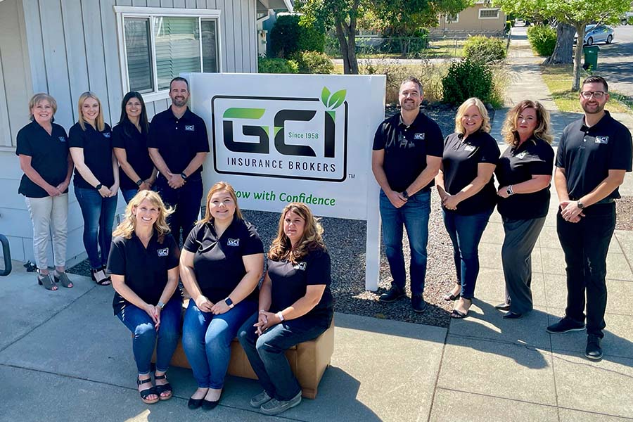 About Our Agency - Portrait of GCI Insurance Brokers Staff Outside the Office Building Next to a Sign with the GCI Logo